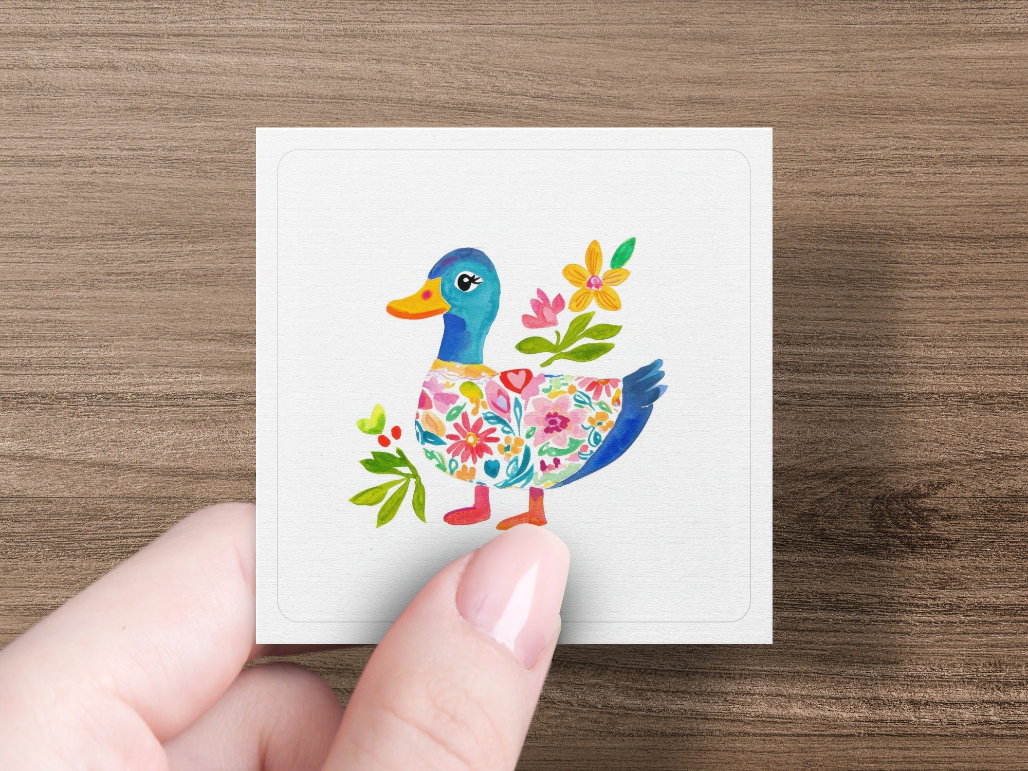 Whimsical duck illustration with floral patterns on a white card held by a person's fingers.