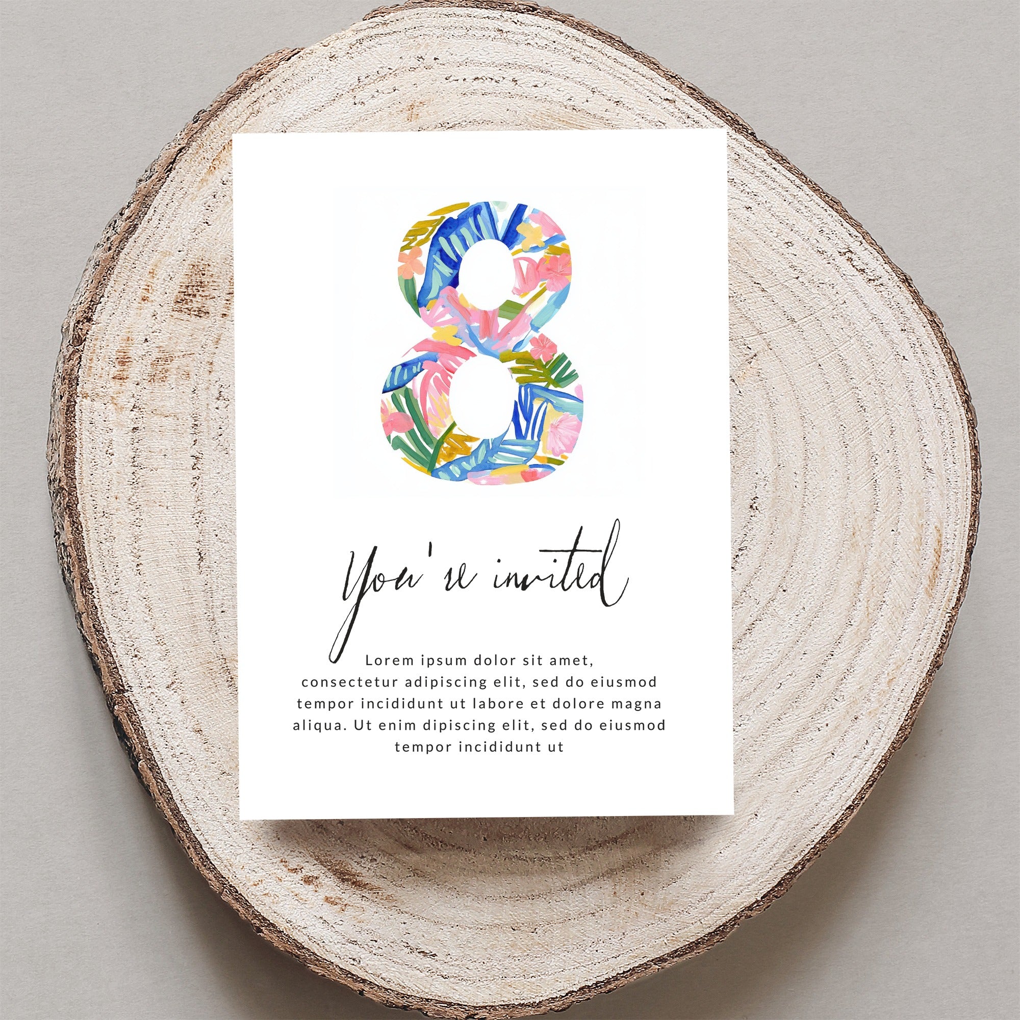 Card with "You're invited" and floral "8" on wood slice.
