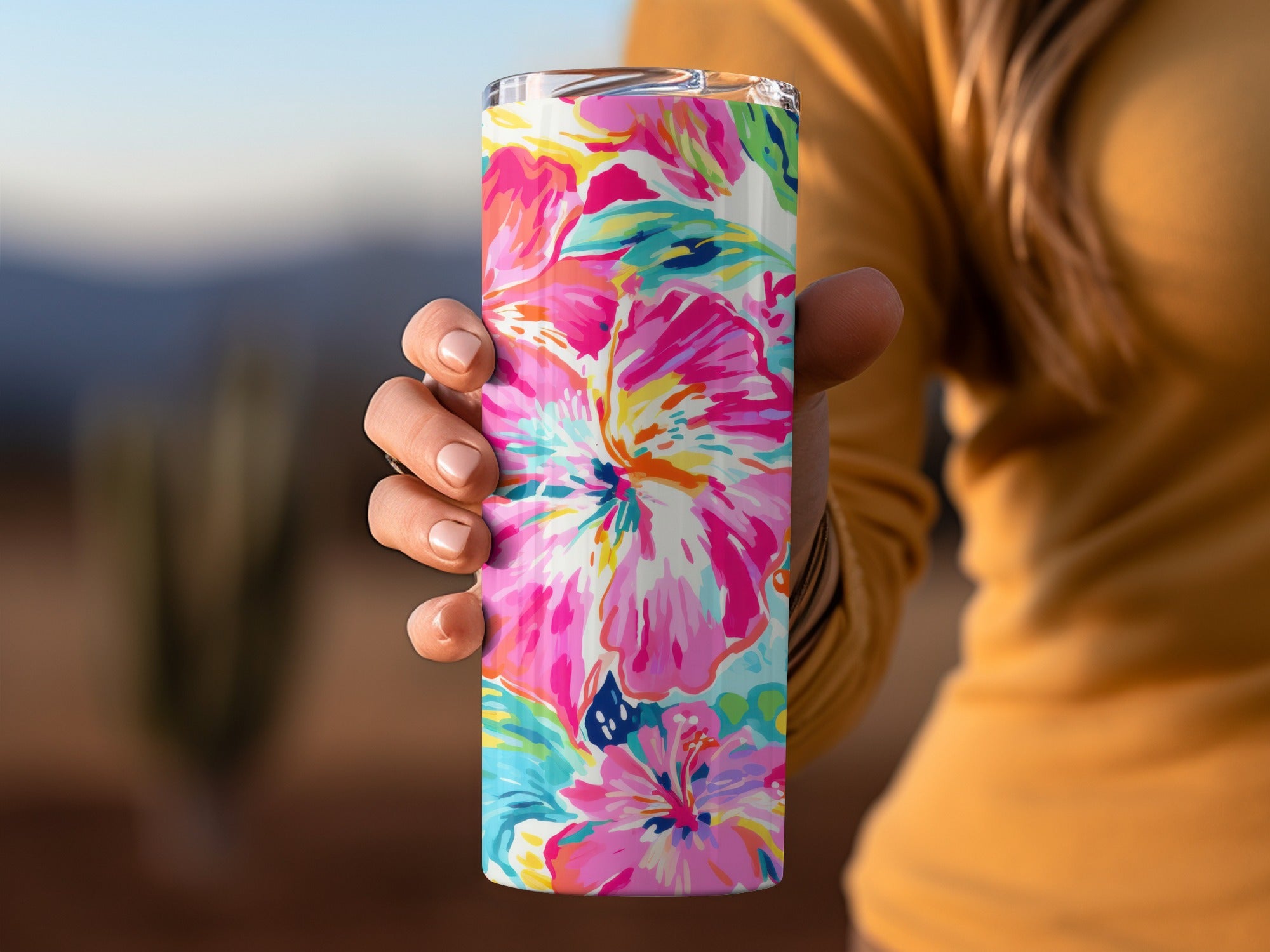 Colorful floral pattern on a tall, stainless steel tumbler held by a hand.