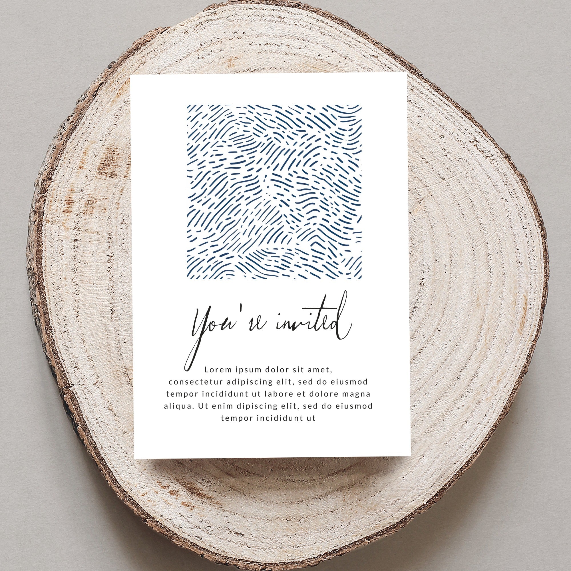 Invitation card with "You're invited" and placeholder text on wood slice.