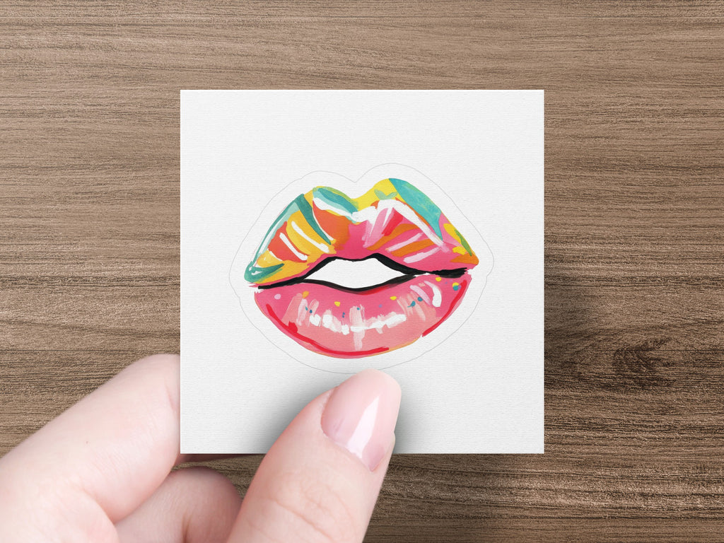 Colorful, stylized lips sticker held by a hand with painted nails.