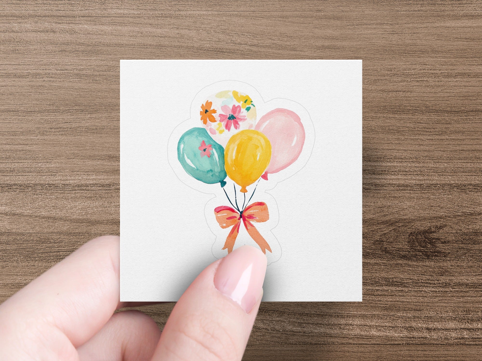 Hand holding a cluster of colorful balloons tied with an orange ribbon.
