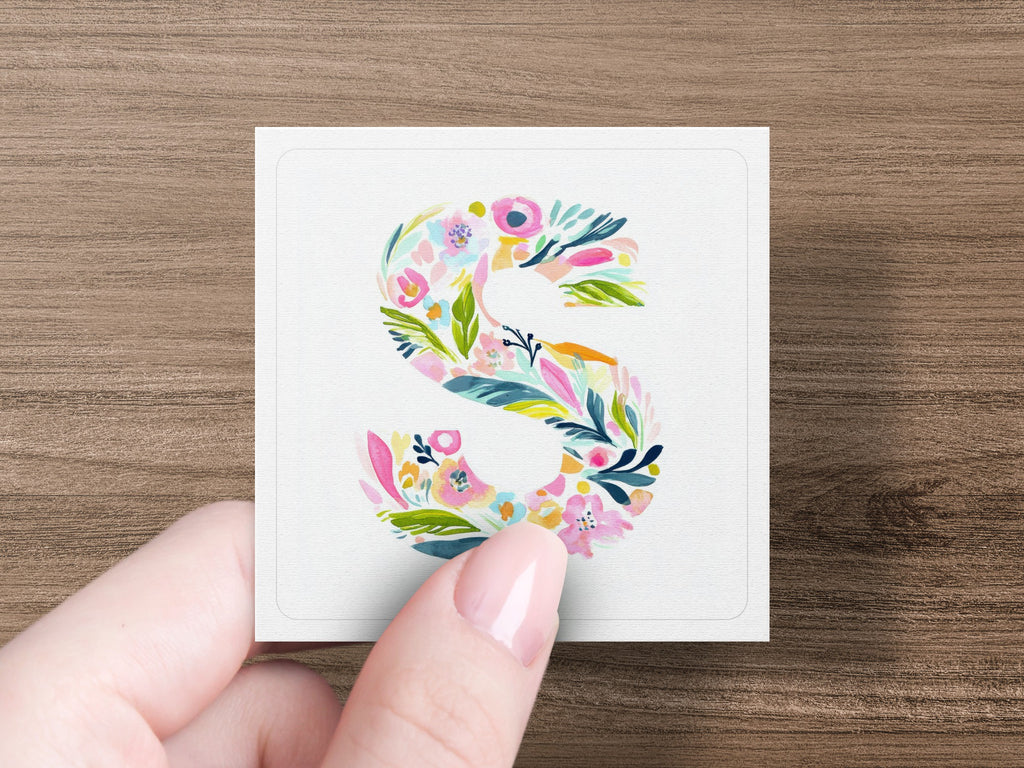 Floral letter S on a card held by a hand.