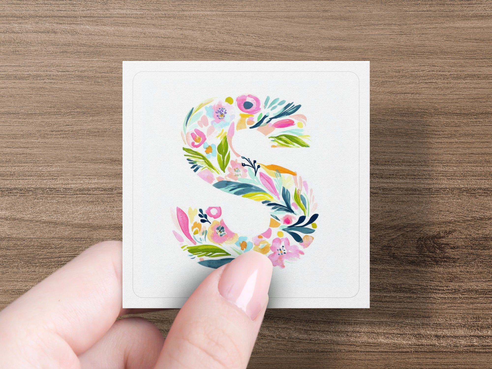 Floral letter S on a card held by a hand.