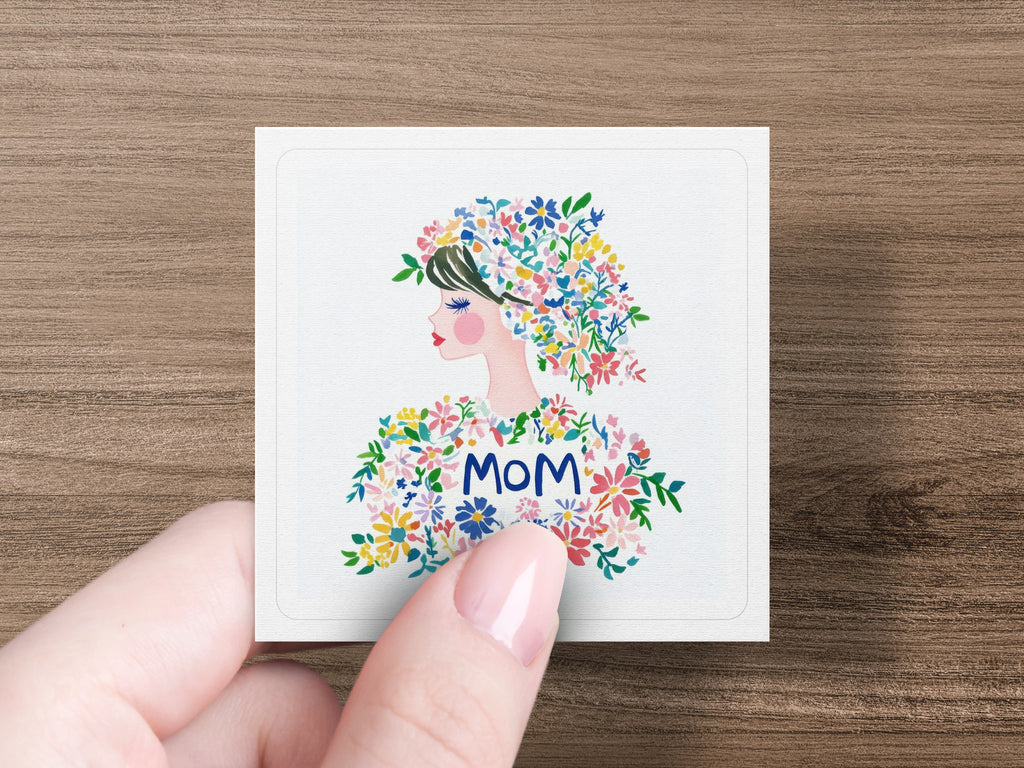 Illustration of a woman with colorful flowers in her hair, the word "MOM" prominent.