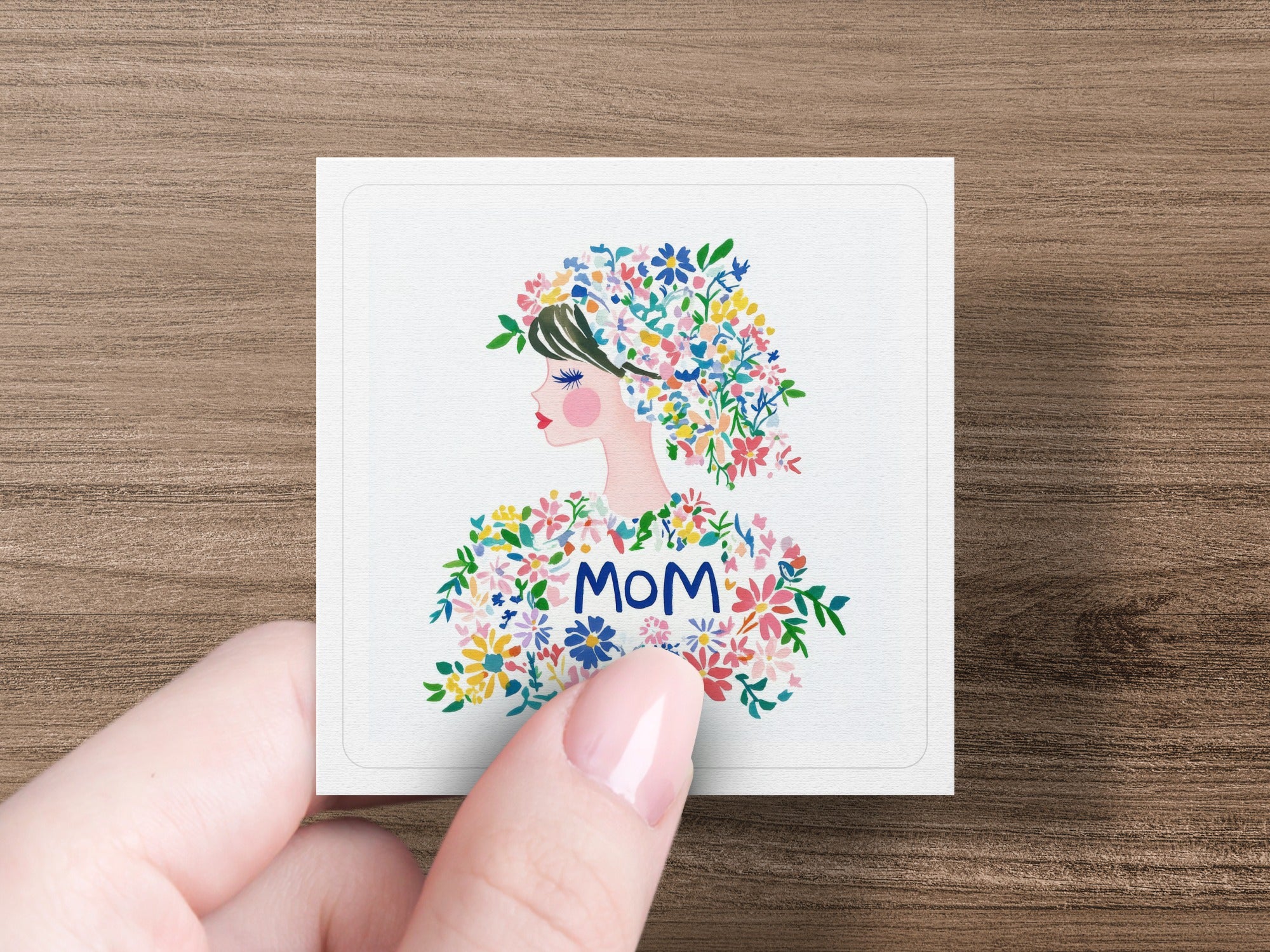 Illustration of a woman with colorful flowers in her hair, the word "MOM" prominent.