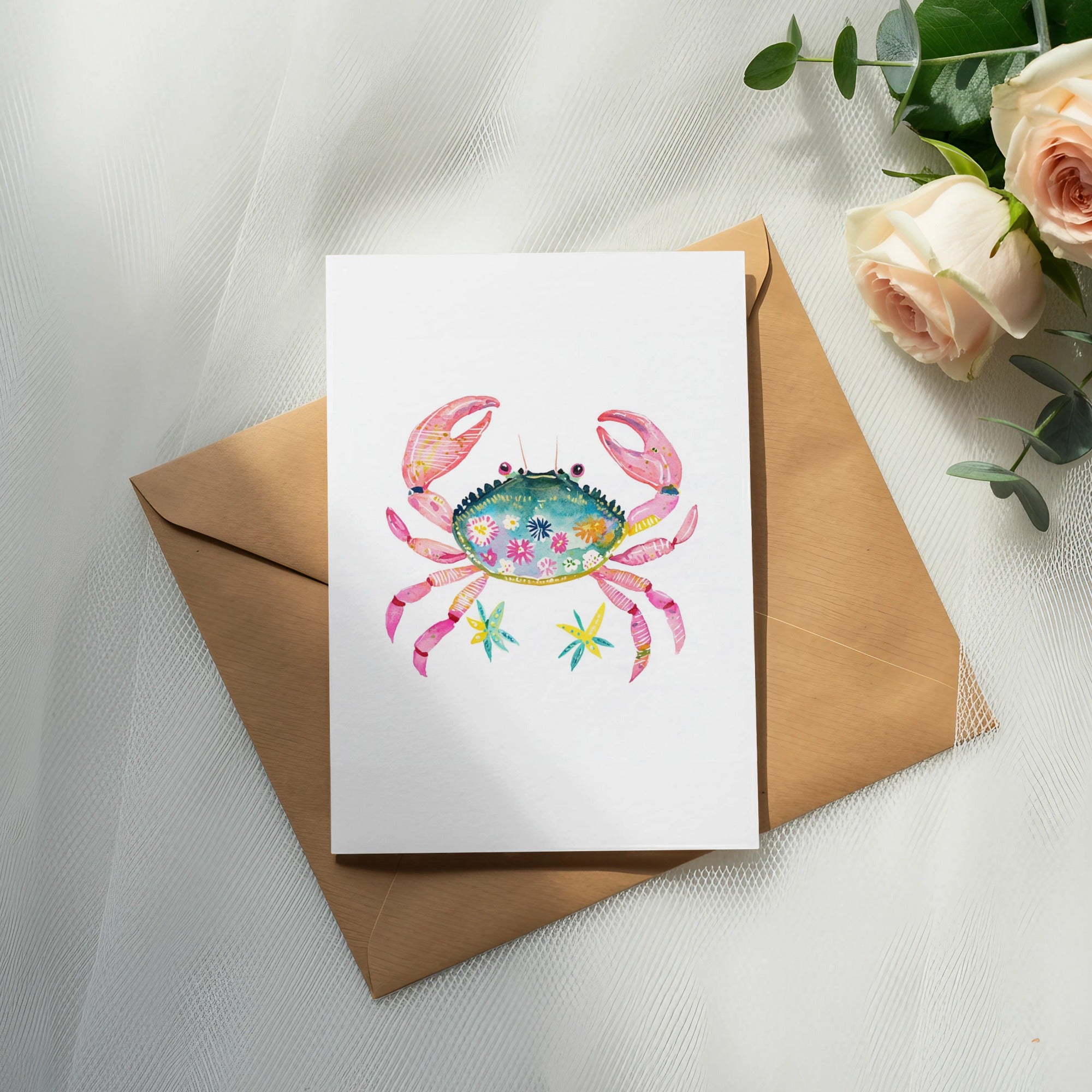 Watercolor crab illustration with floral accents on a card atop a kraft envelope.