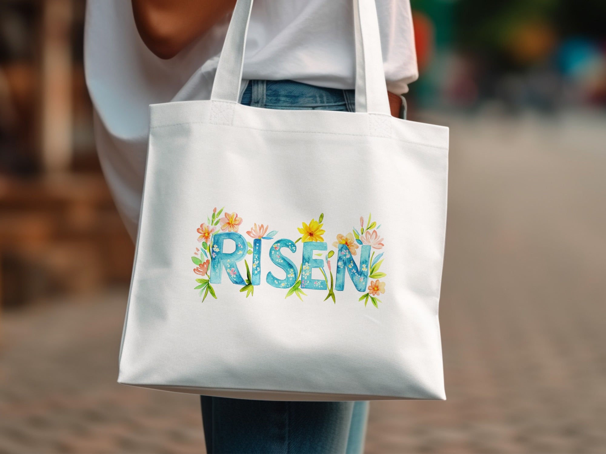 White tote bag with "RISEN" text surrounded by watercolor flowers and leaves.