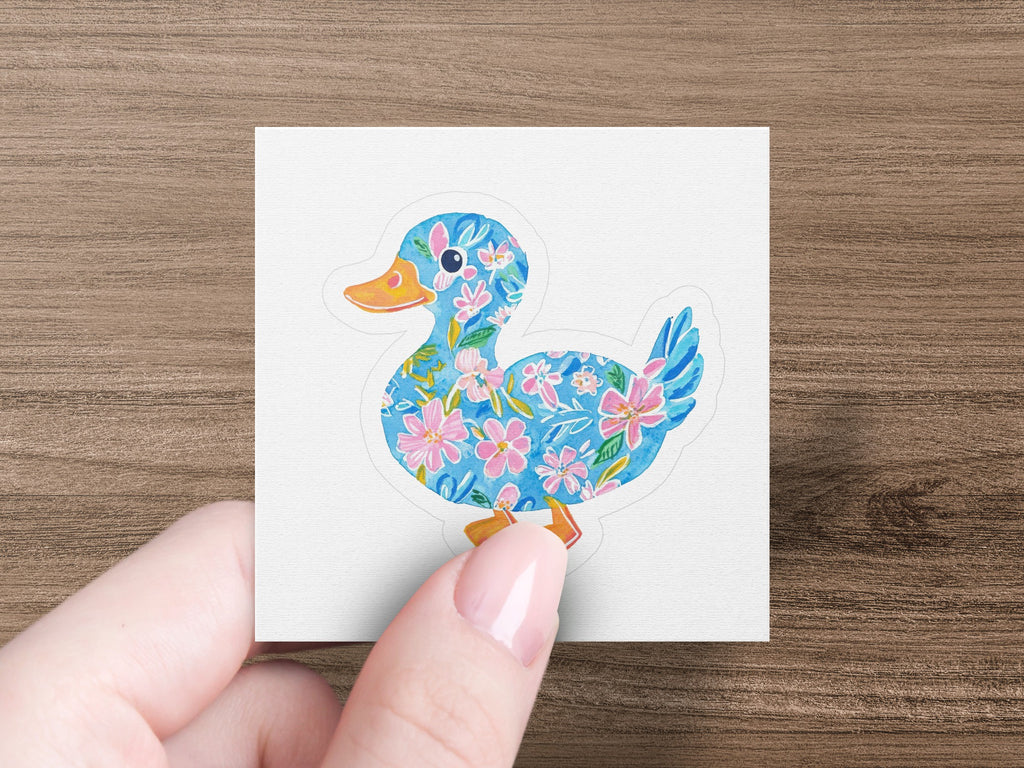Blue duck sticker with pink floral pattern held by fingers.