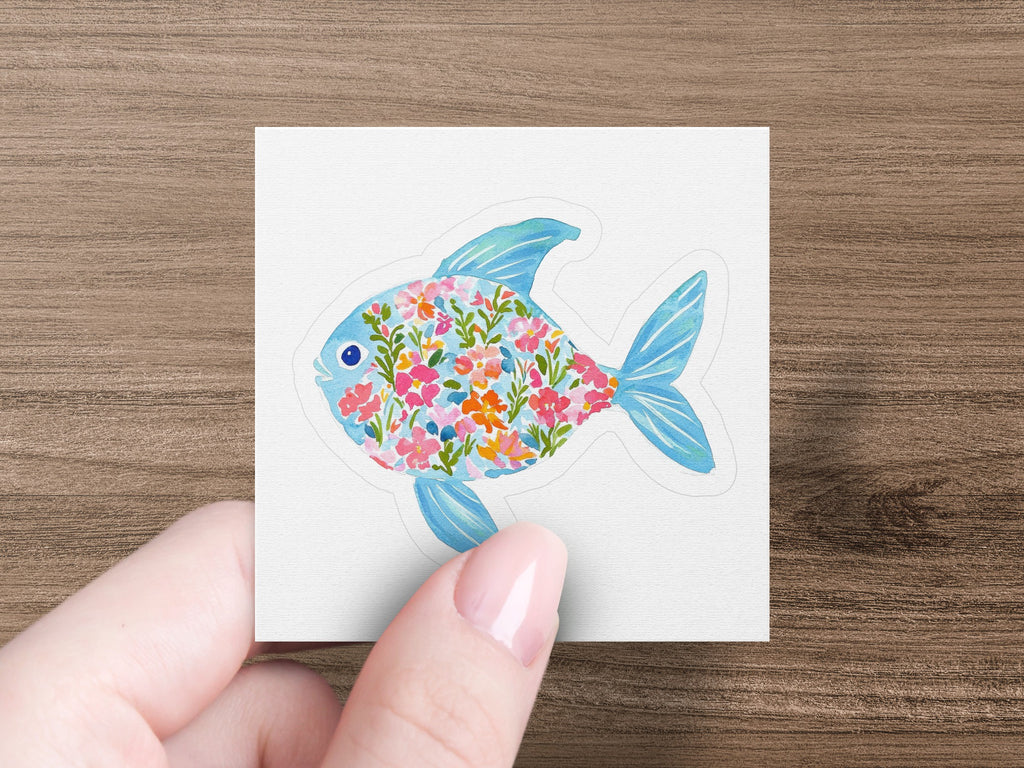 Fish sticker filled with colorful floral patterns, held by fingers.