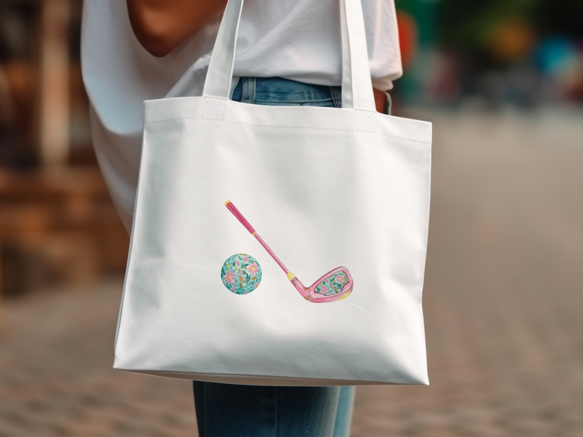 White tote bag with pink golf club and floral golf ball illustration.