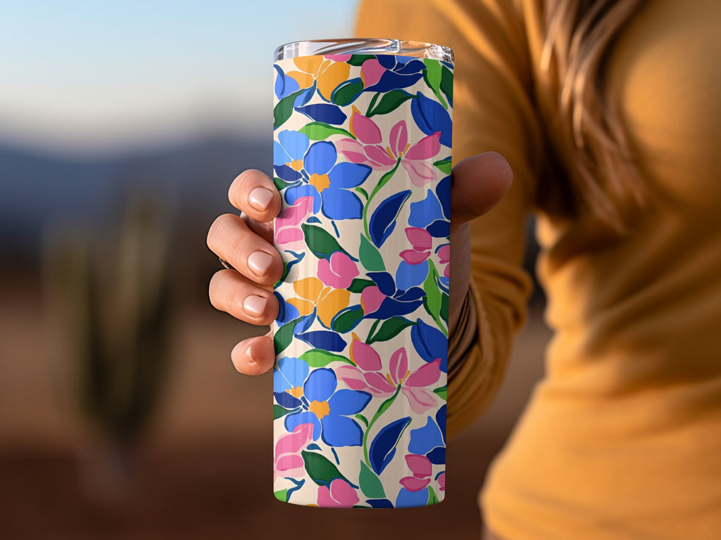 Hand holding a floral tumbler with blue, pink, and yellow flowers.