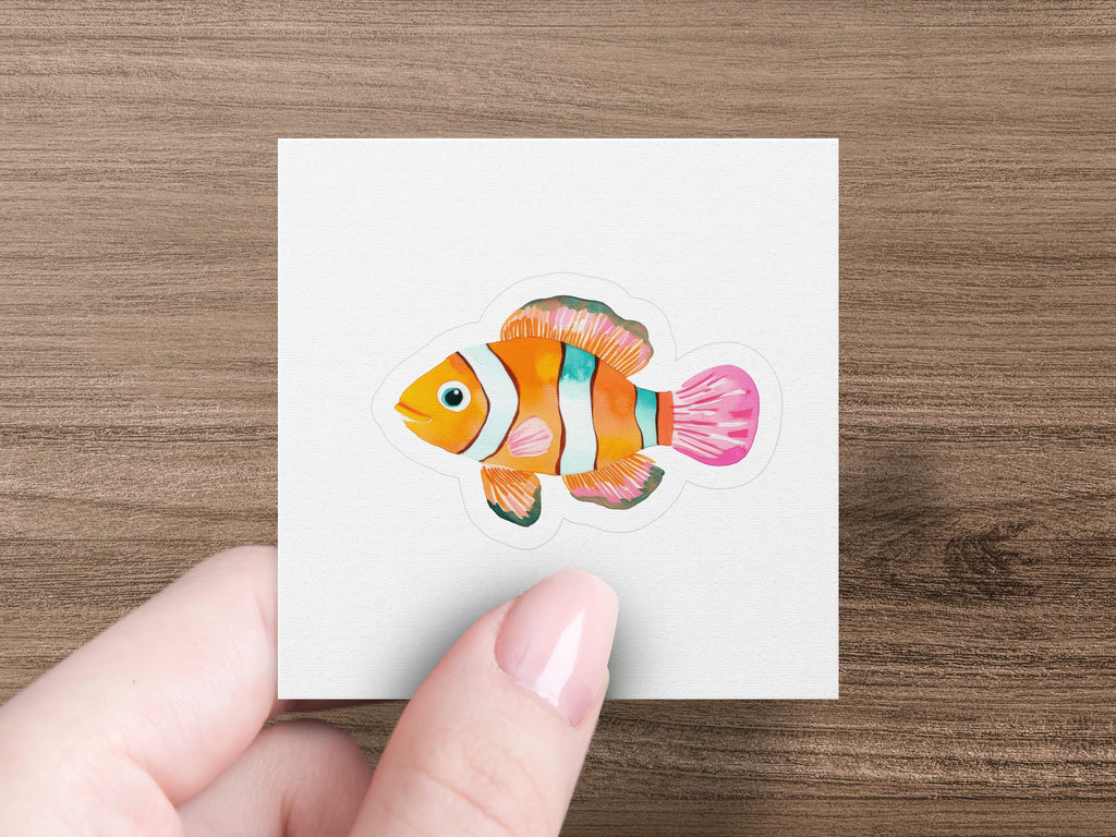 Hand holding a sticker of an orange and white striped clownfish.