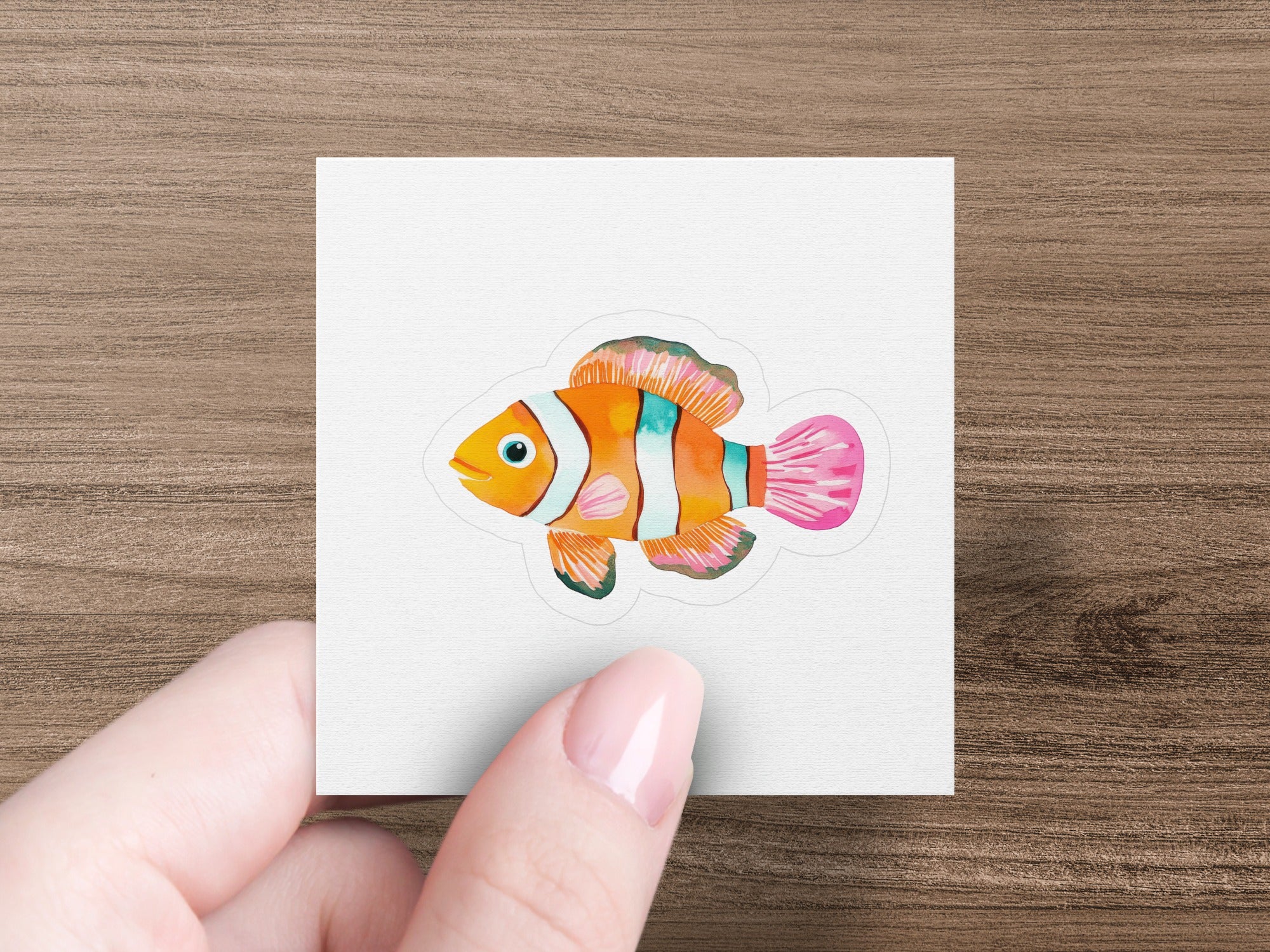 Hand holding a sticker of an orange and white striped clownfish.