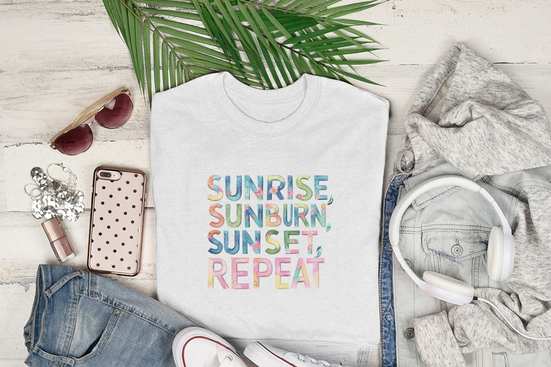 White t-shirt with "Sunrise, Sunburn, Sunset, Repeat" graphic, laid flat with clothing and sunglasses.