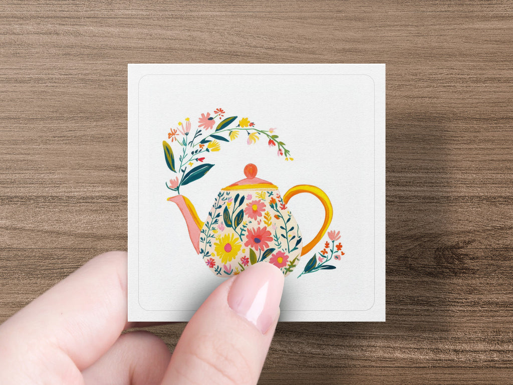 Floral teapot with pink lid on white card held by fingers.
