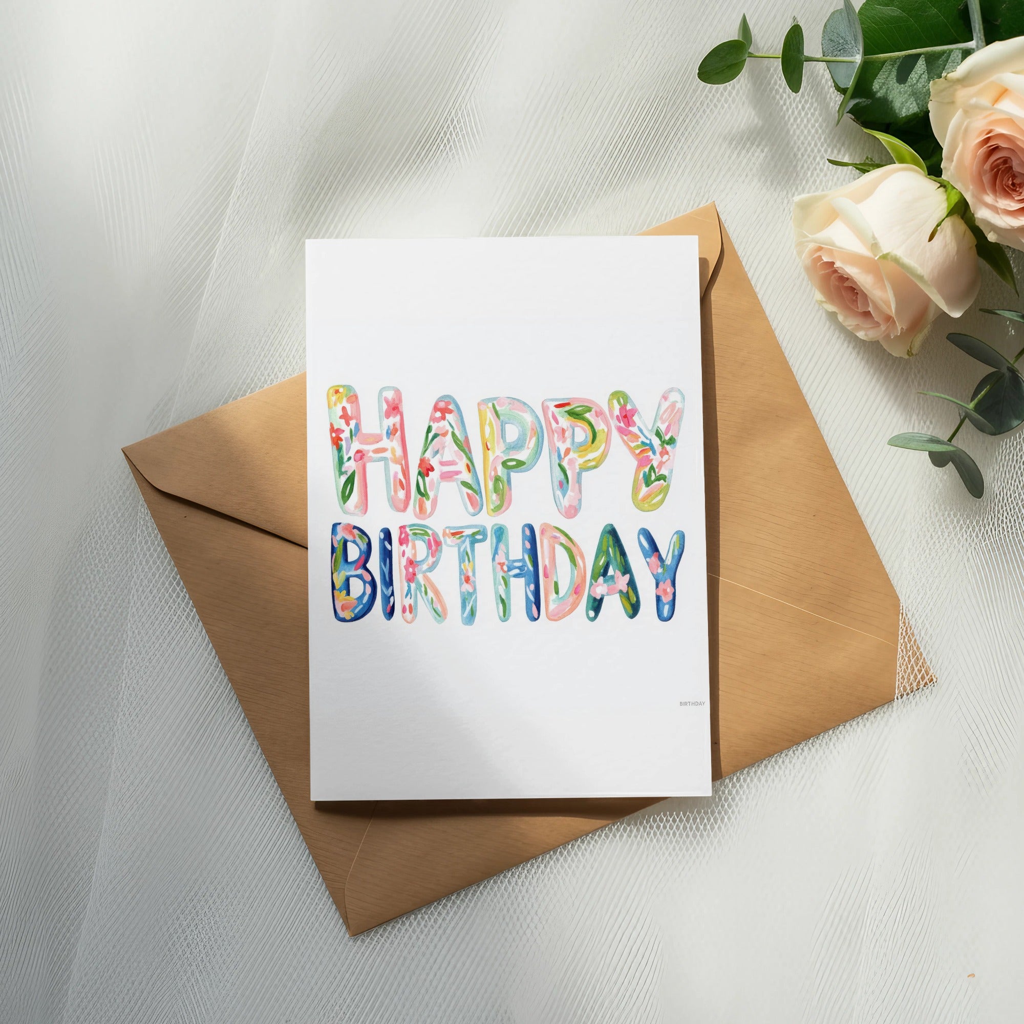 Watercolor "Happy Birthday" lettering on a card with a kraft envelope and roses.