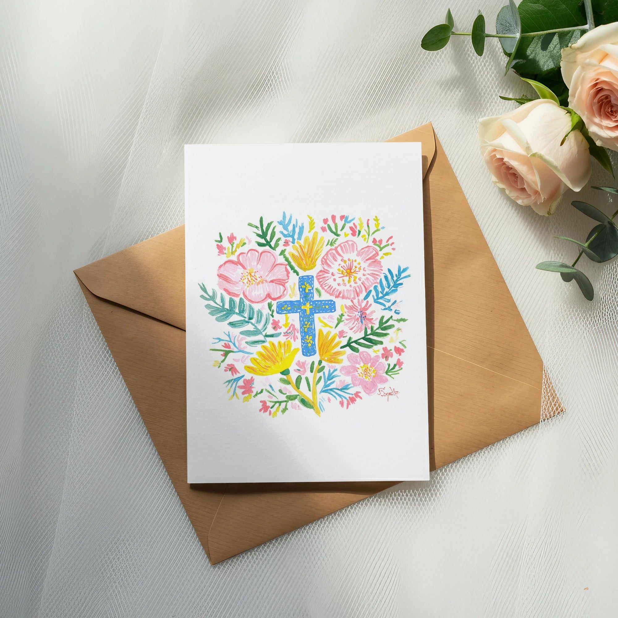 Card with floral watercolor cross design on brown envelope with roses and eucalyptus.
