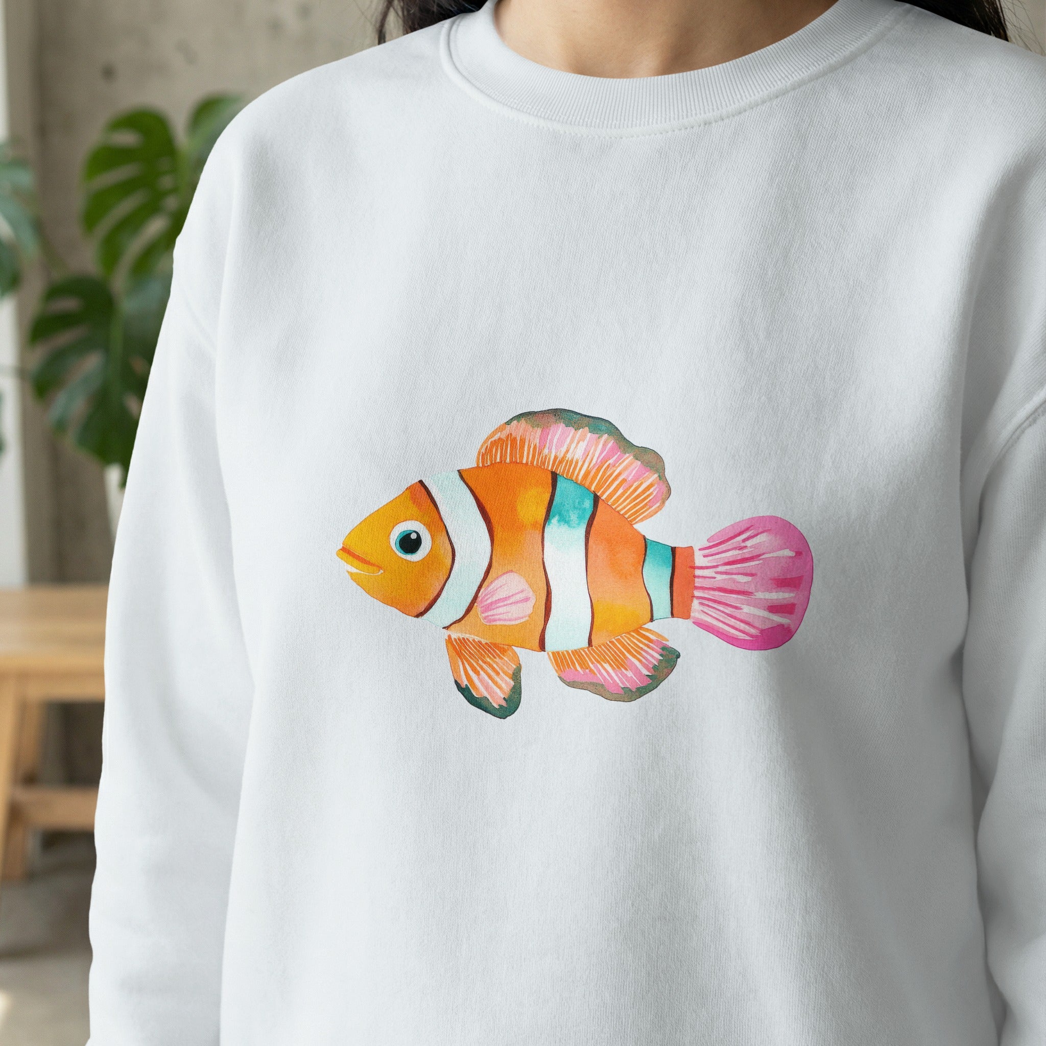 Watercolor clownfish graphic on a white crewneck sweatshirt.