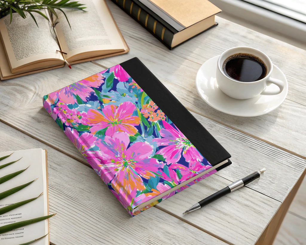 Floral notebook with black spine and a pen beside coffee and books.