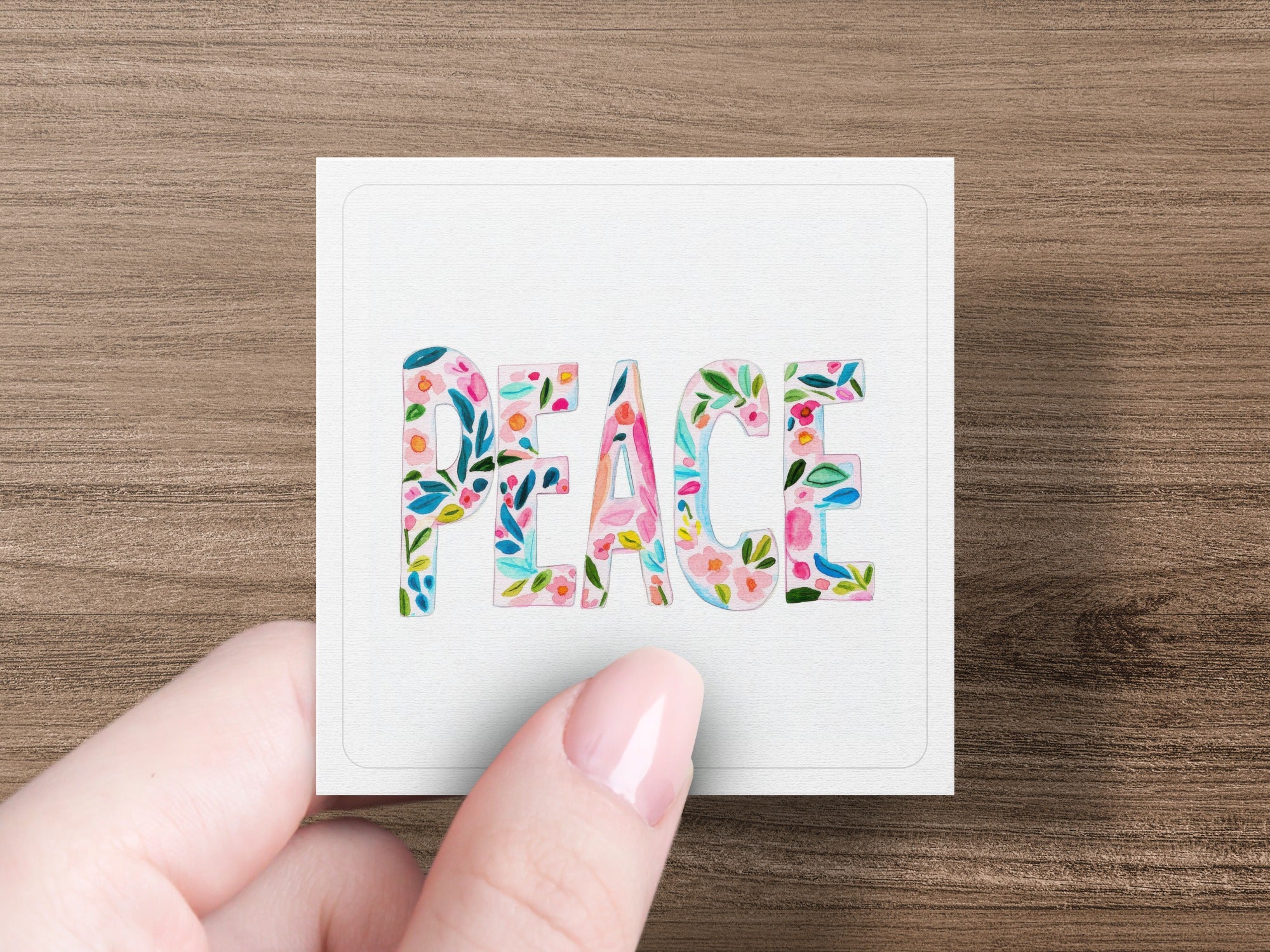 Hand holding card with "PEACE" in floral lettering