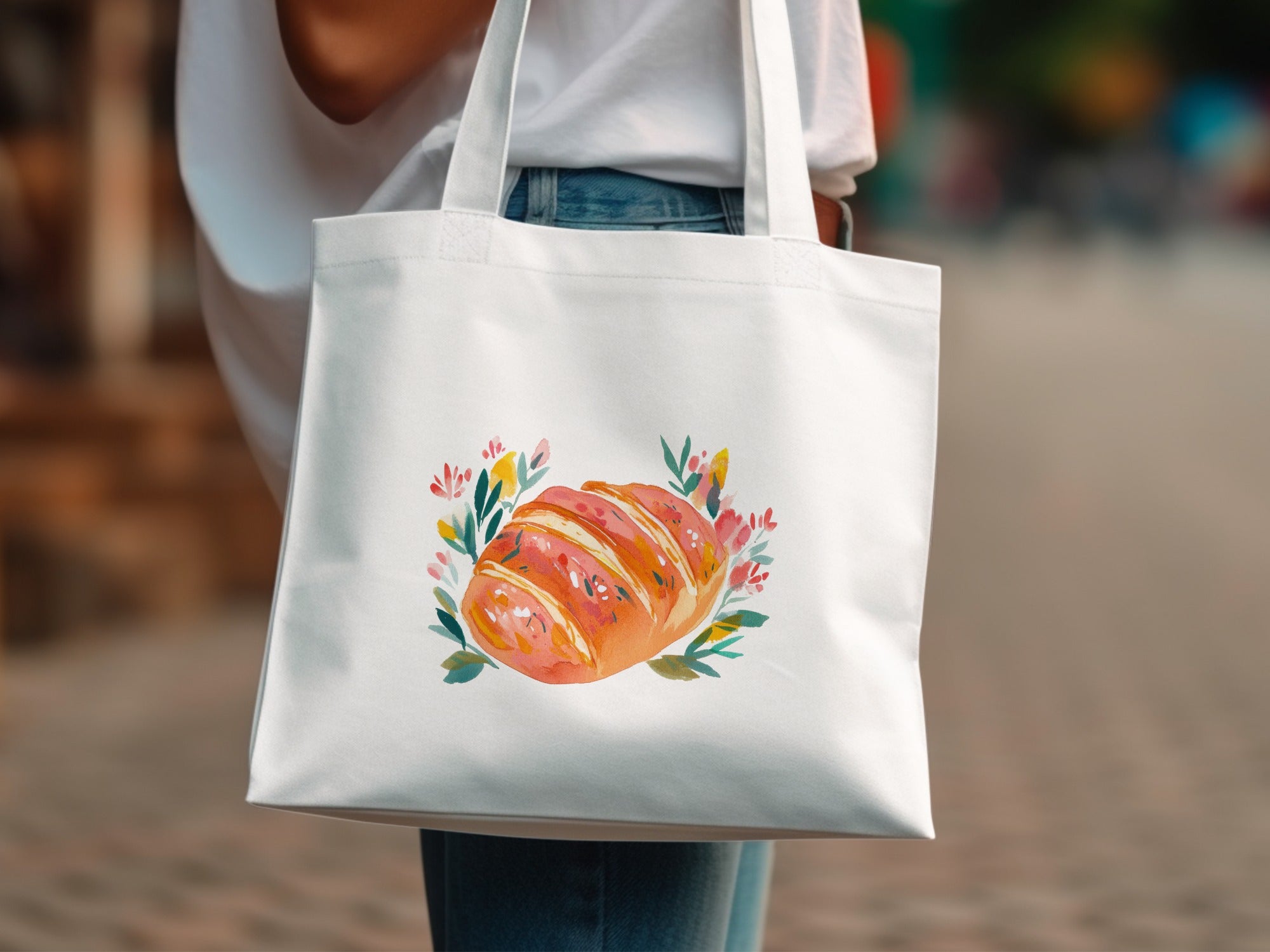 White tote bag with watercolor illustration of a croissant surrounded by flowers.