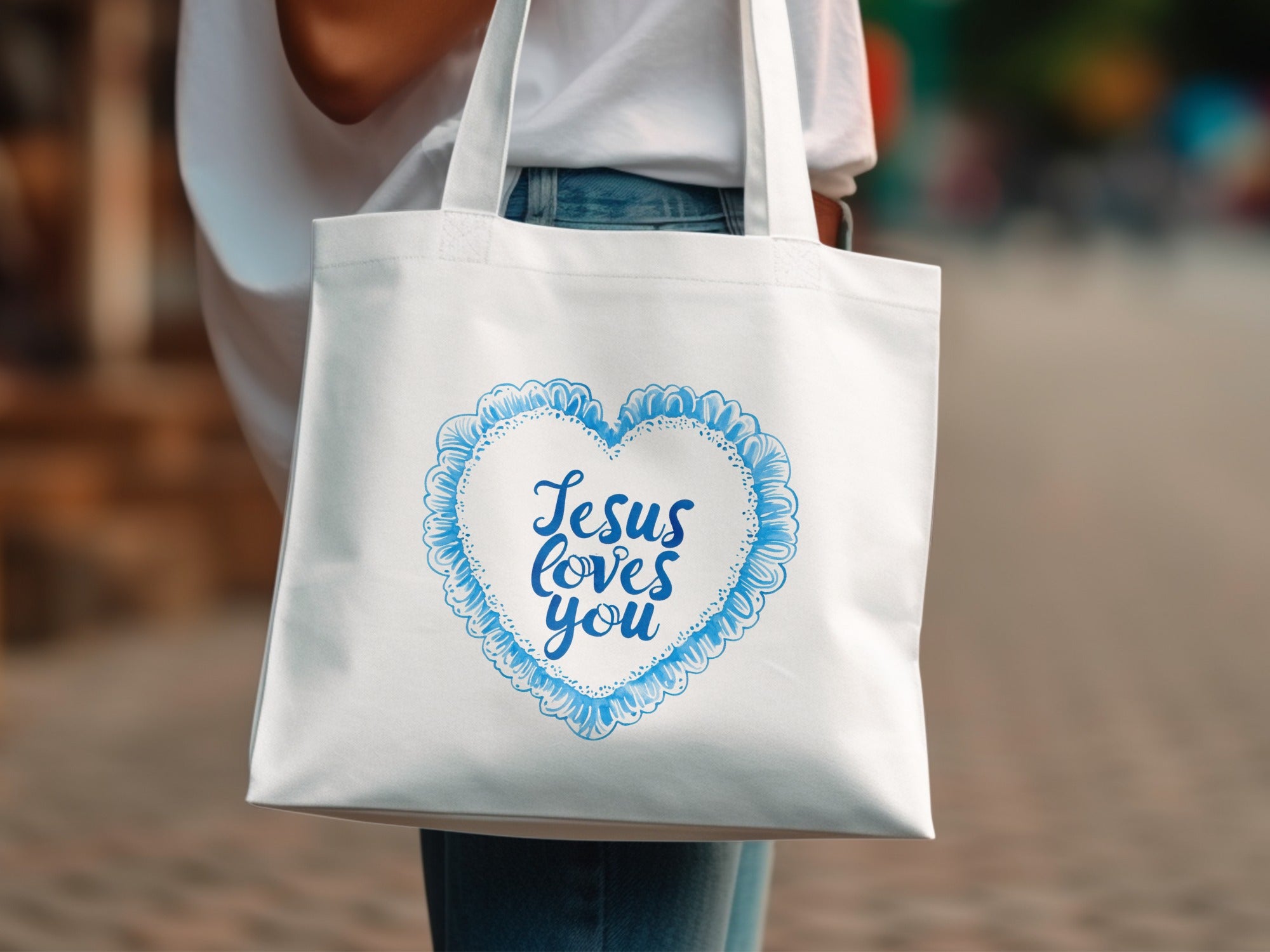 White tote bag with blue heart design and "Jesus loves you" text.