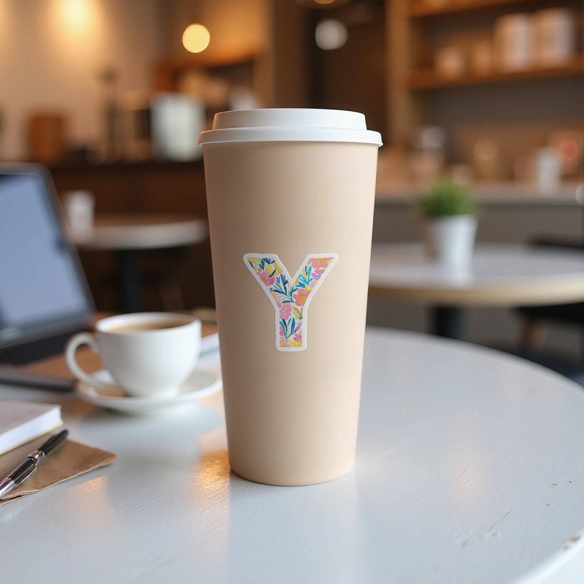 A light tan coffee cup with a floral letter Y sticker on a white table.