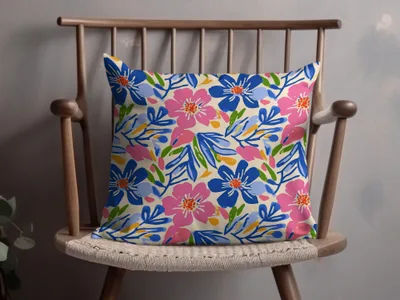 Floral patterned throw pillow with pink and blue flowers on a wooden chair.