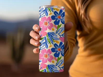 Tan tumbler with pink and blue floral pattern held by hand.