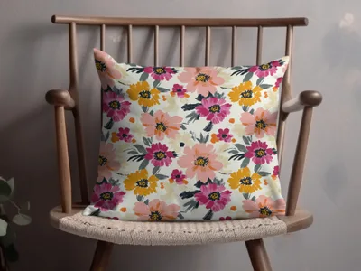 Floral accent pillow with pink, yellow, and orange flowers on a light background.
