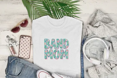White t-shirt with "BAND MOM" in floral letters, displayed with jeans and headphones.