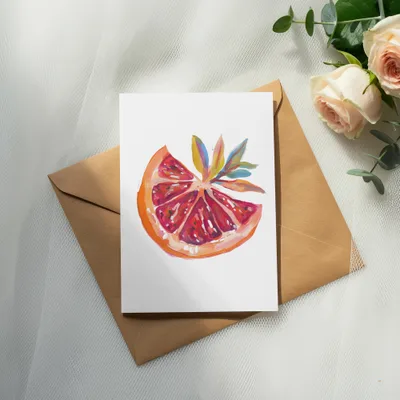 Watercolor painting of a grapefruit slice on a card, next to roses and eucalyptus.