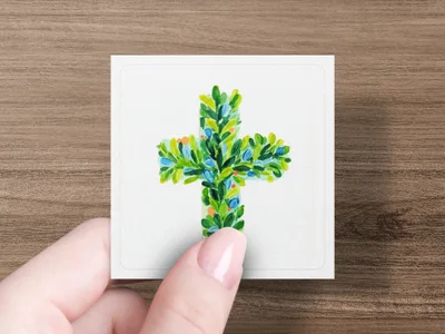Hand holding a small square card with a painted green cross adorned with blue berries.