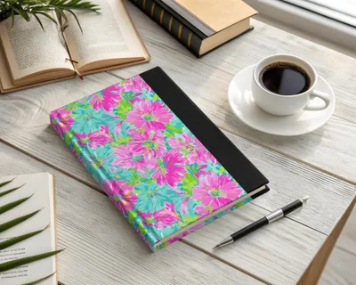 Floral patterned notebook with black spine and pen on desk.