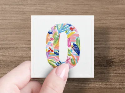 Hand holds square card with colorful floral letter O design.