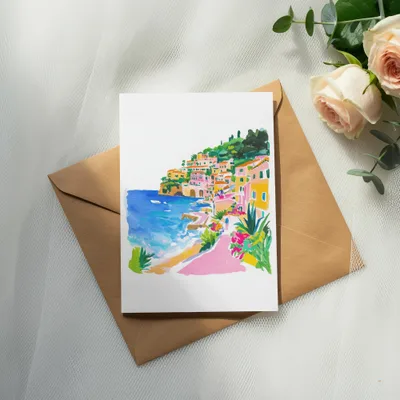 Watercolor painting of a Mediterranean village on a postcard, resting on an envelope.