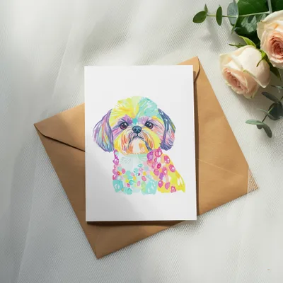 Watercolor portrait of a colorful dog on a card atop a brown envelope.