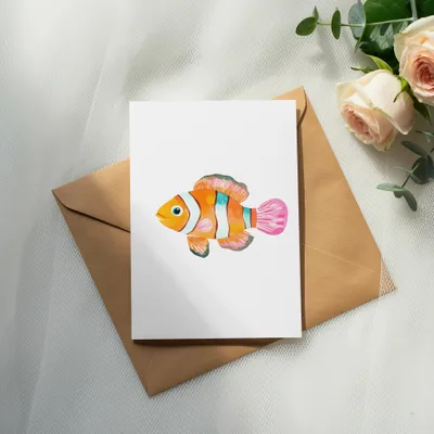 Watercolor clownfish illustration on a card placed on an envelope with roses.