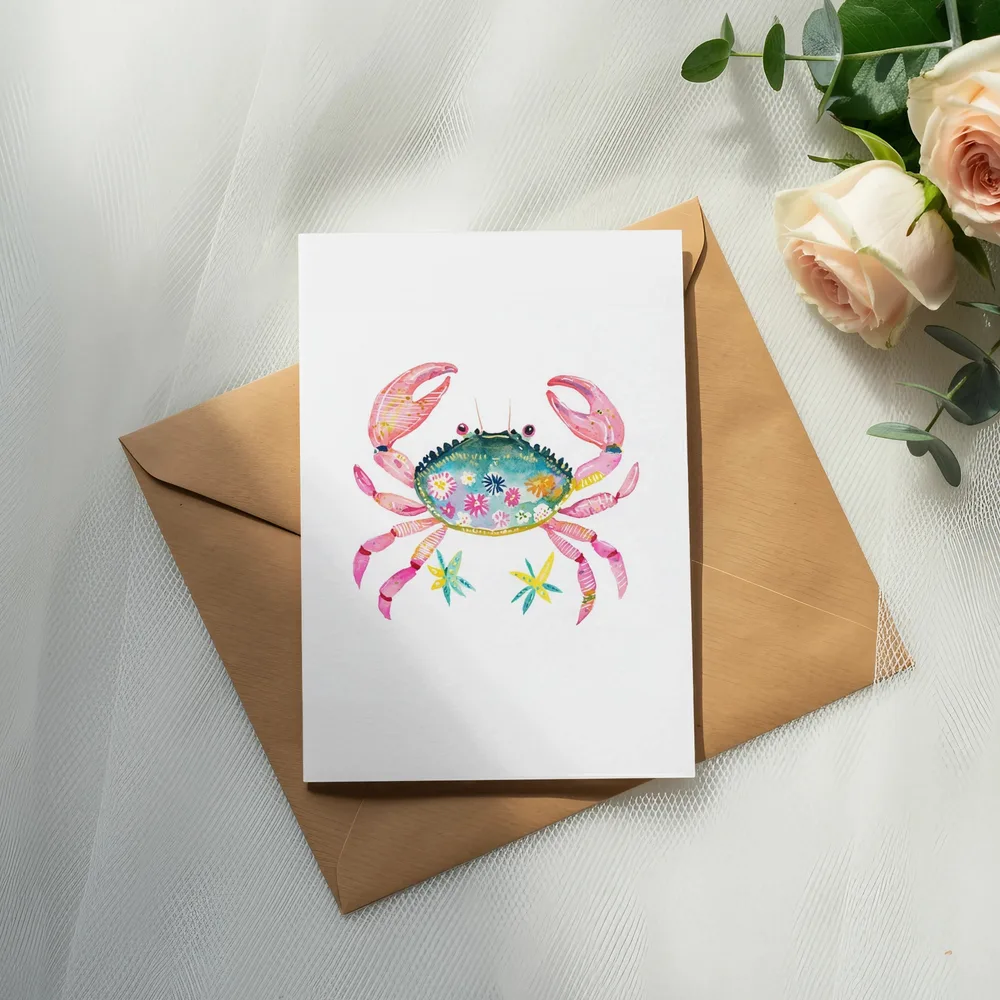 Watercolor crab illustration with floral accents on a card atop a kraft envelope.