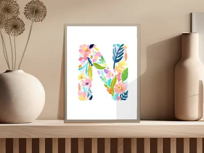 Watercolor floral letter N in a frame on a shelf.