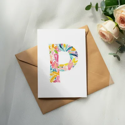 Card with colorful floral letter P on brown envelope, with roses and eucalyptus.