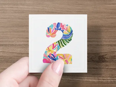 Hand holding square with colorful floral number 2.