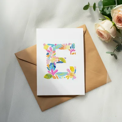 White card with colorful floral letter 'E' on a kraft envelope.