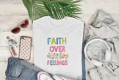 White t-shirt with "FAITH OVER FEELINGS" text and floral design.