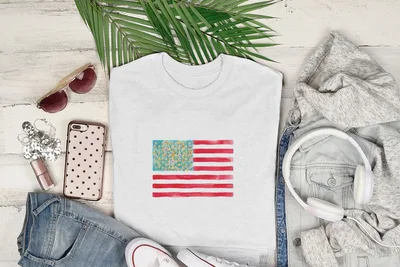 White t-shirt with watercolor American flag design and surrounding clothing.