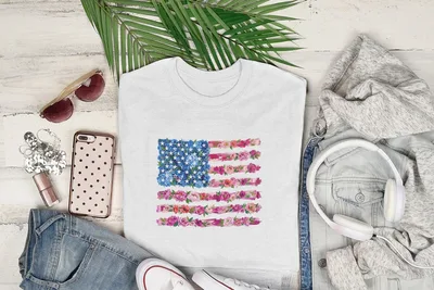 White t-shirt with floral American flag design, styled with jeans, sunglasses, and headphones.
