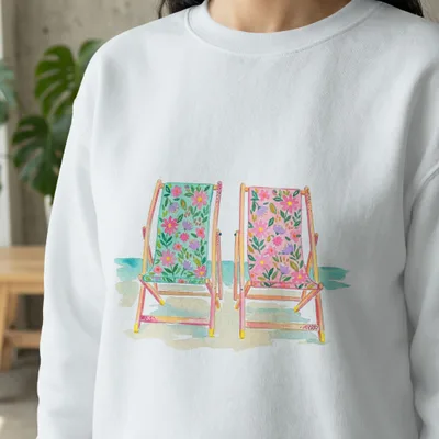 Watercolor illustration of two floral deck chairs on a beach.