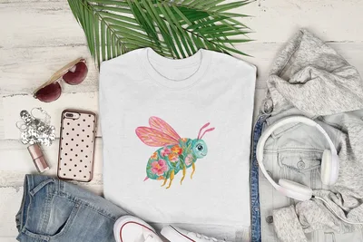 White t-shirt with a colorful floral bee graphic, laid flat with clothing and accessories.