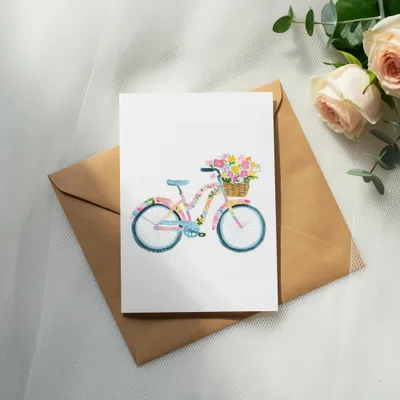 Watercolor bicycle with floral basket on brown envelope and roses.
